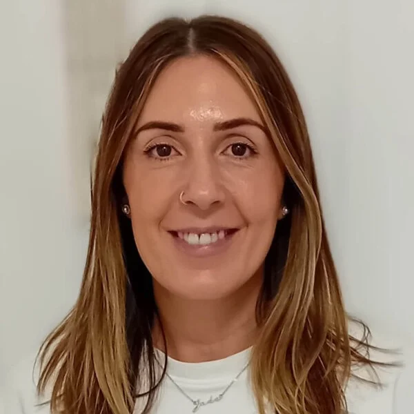 Portrait of a woman with brown hair, wearing a necklace and earrings, smiling at the camera.
