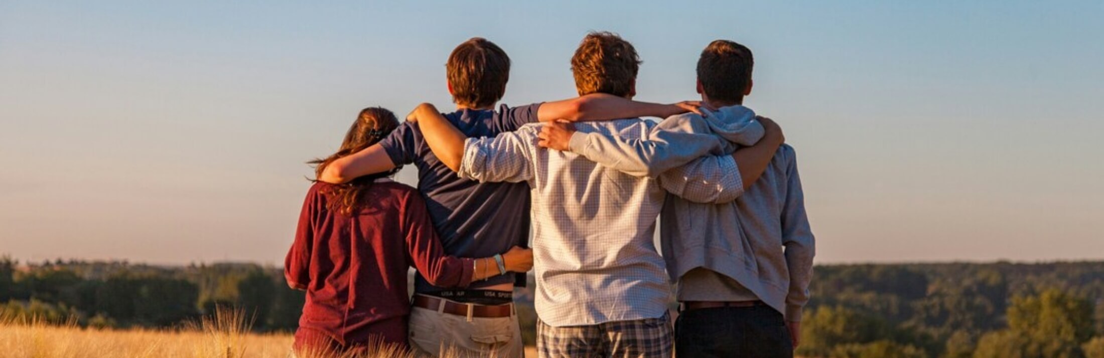 Group of friends with arms around each other, backs to the camera.