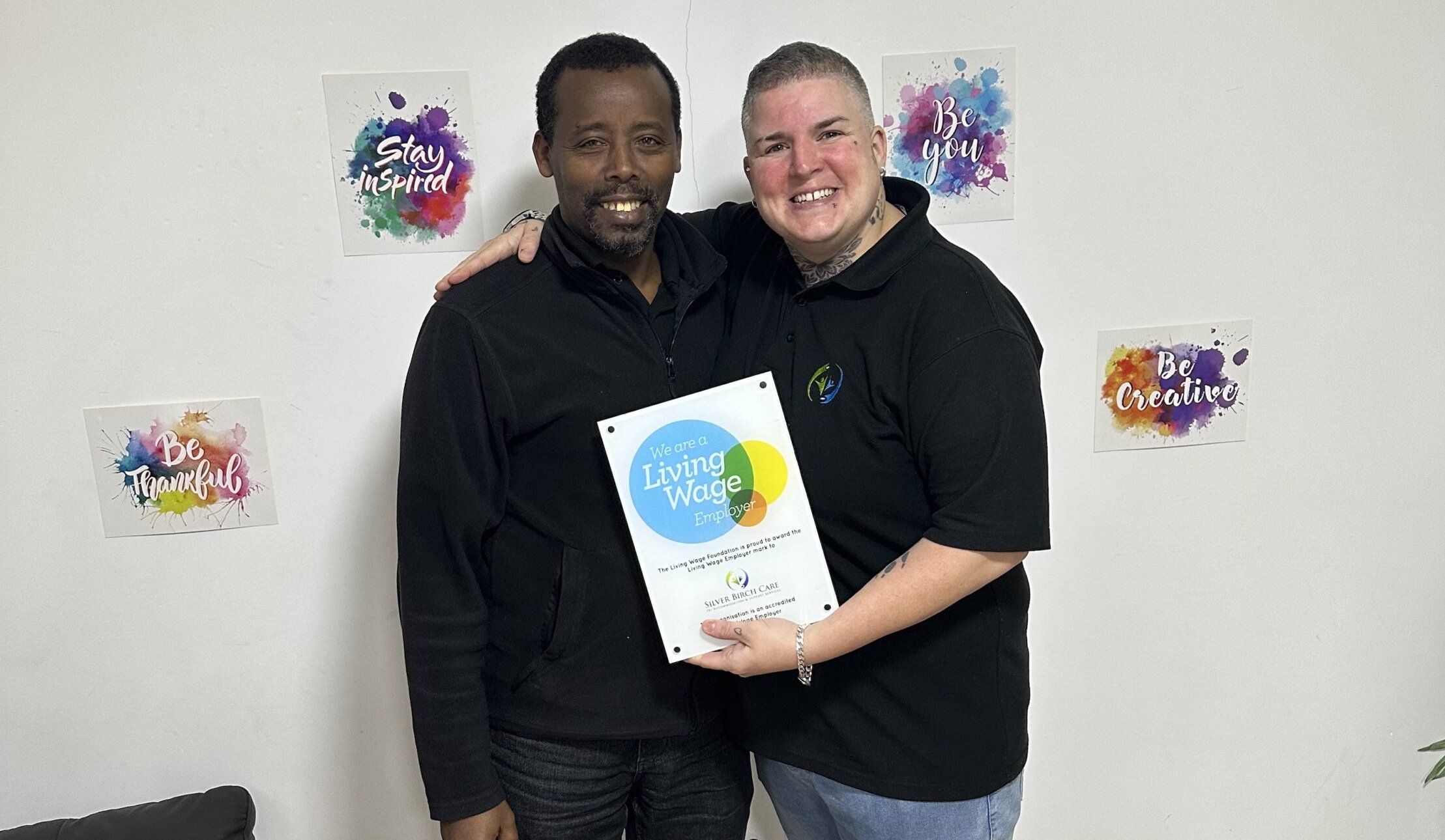 Two people holding a "Living Wage Employer" certificate.