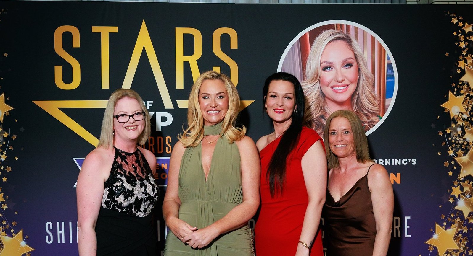 Four women in elegant evening wear standing together in front of a Stars of the Year backdrop.